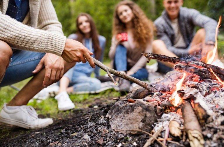 Teenagers camping in nature, sitting at bonfire.